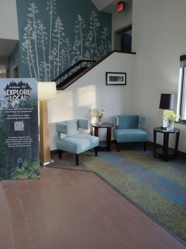 A lobby with a staircase, two blue armchairs, a small table with a vase, and a poster advertising local trails.