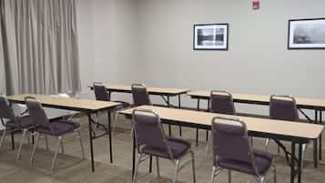 A conference room with long tables and chairs, a fire alarm on the wall, and two framed pictures.