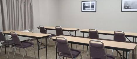 A conference room with long tables and chairs, a fire alarm on the wall, and two framed pictures.