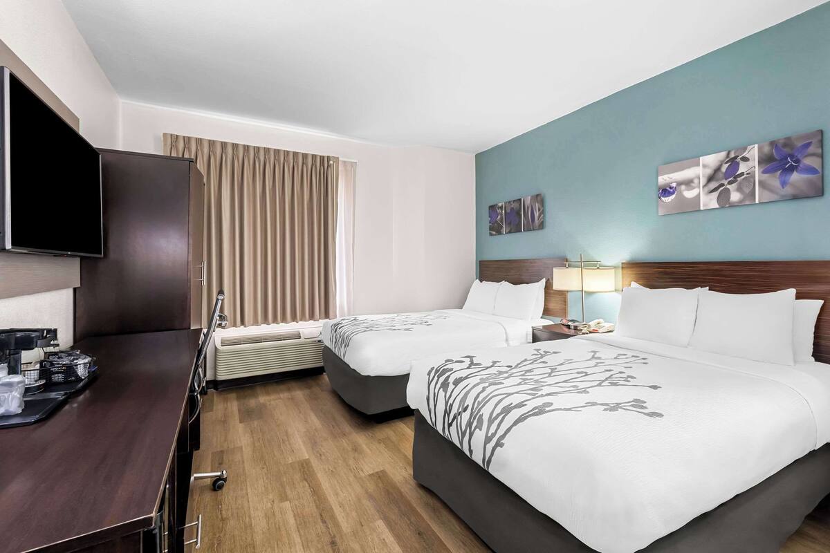 A hotel room with two beds, a flat-screen TV, a desk with a coffee machine, and artwork on the walls.