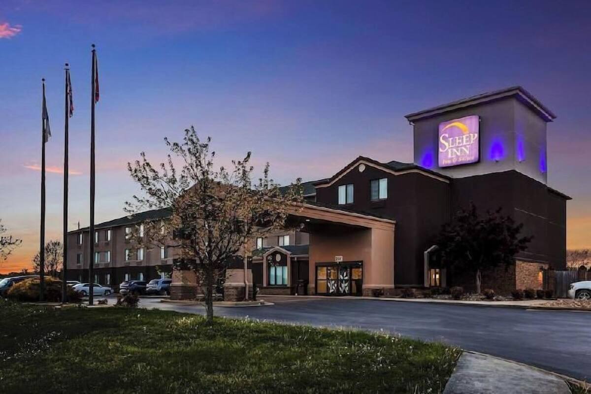 A Sleep Inn hotel with a modern design, a parking lot, and a clear sky.