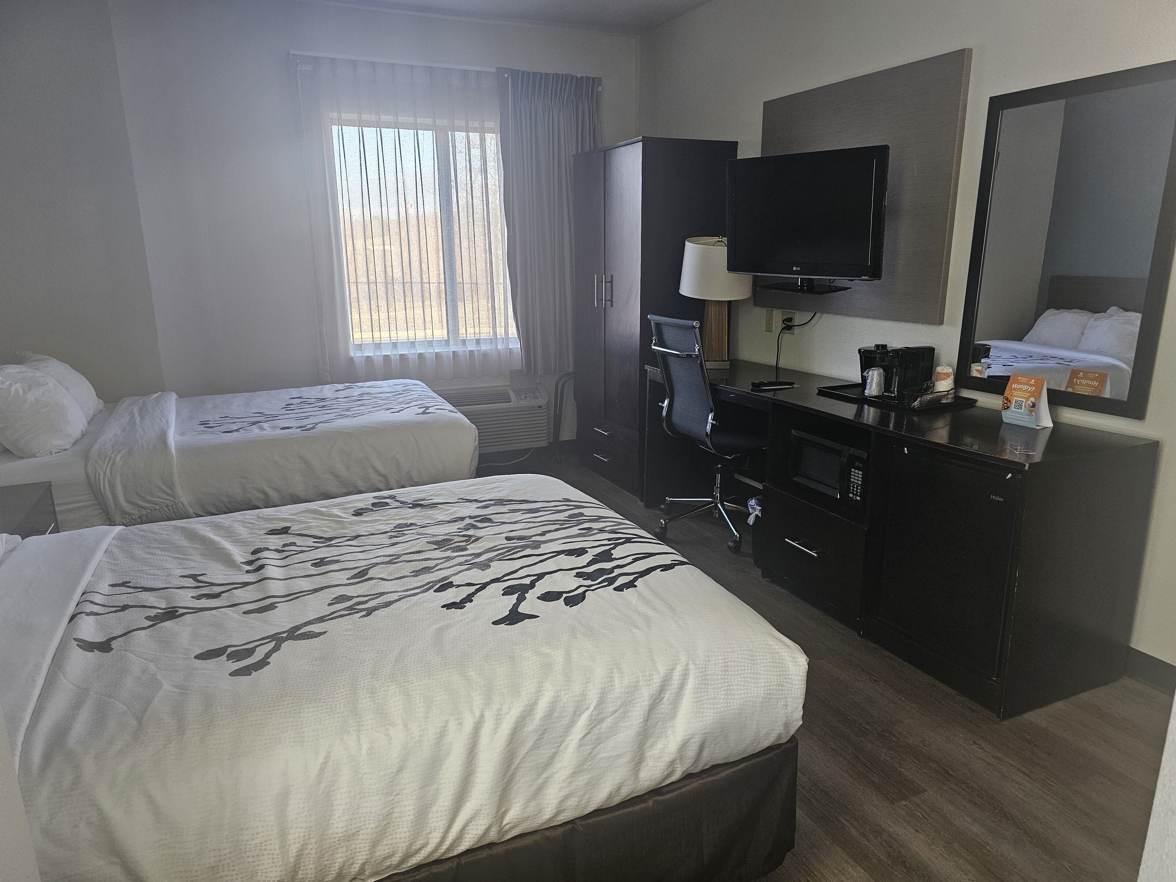 A hotel room with two beds, a desk with a computer, a chair, a TV, and a minibar.