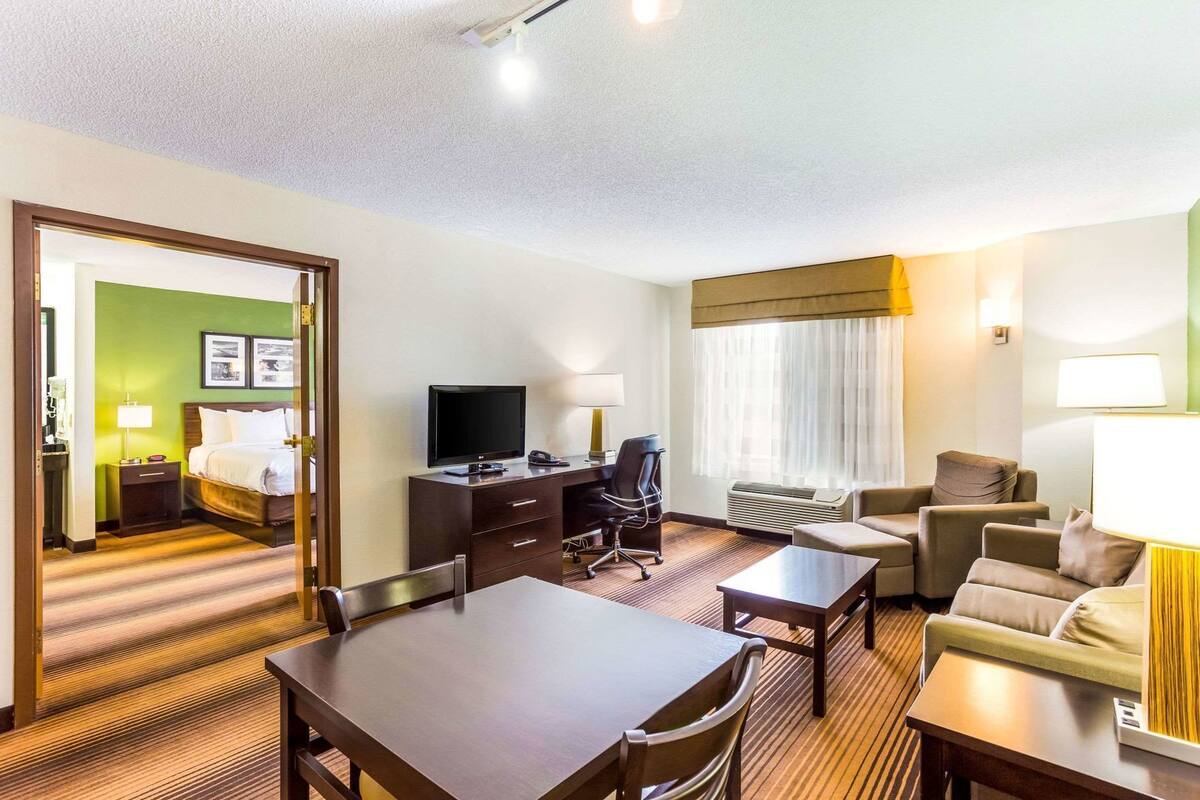 A hotel room with a bed, desk, TV, and seating area.