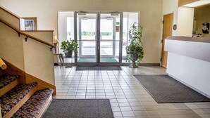 A hotel lobby with a staircase, a reception desk, and a large glass door leading outside. - Rodeway Inn Abbotsford (Colby)