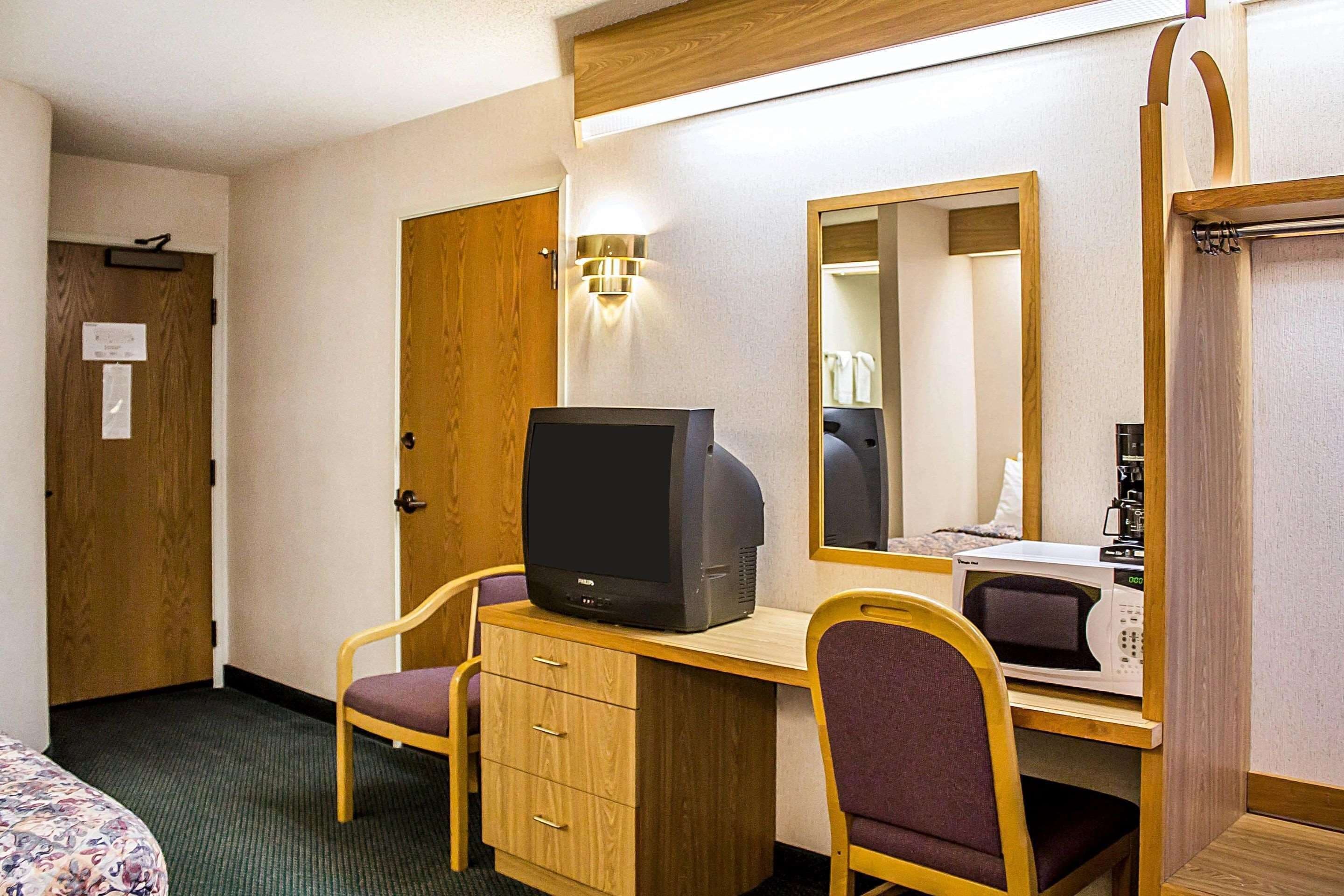 A hotel room with a wooden desk, a television, a microwave, a bed, and a mirror.