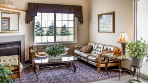 A living room with a fireplace, two sofas, a coffee table, and a large window with a view of trees. - Rodeway Inn Abbotsford (Colby)