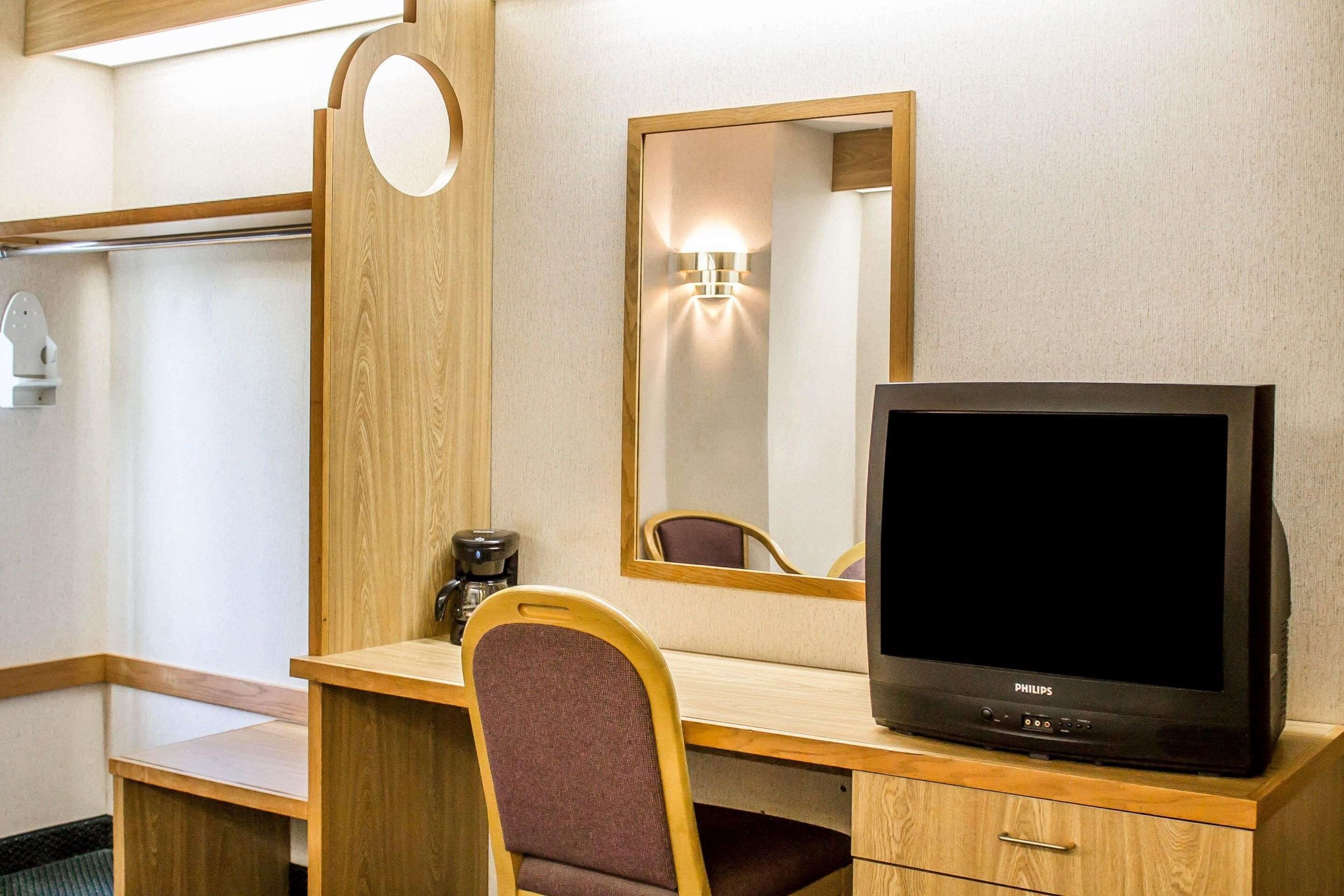 Una habitación de hotel con un escritorio de madera, televisor, silla, espejo y cafetera.