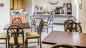 A compact kitchen with wooden cabinets, a central island, and a dining area with chairs. - Rodeway Inn Abbotsford (Colby)