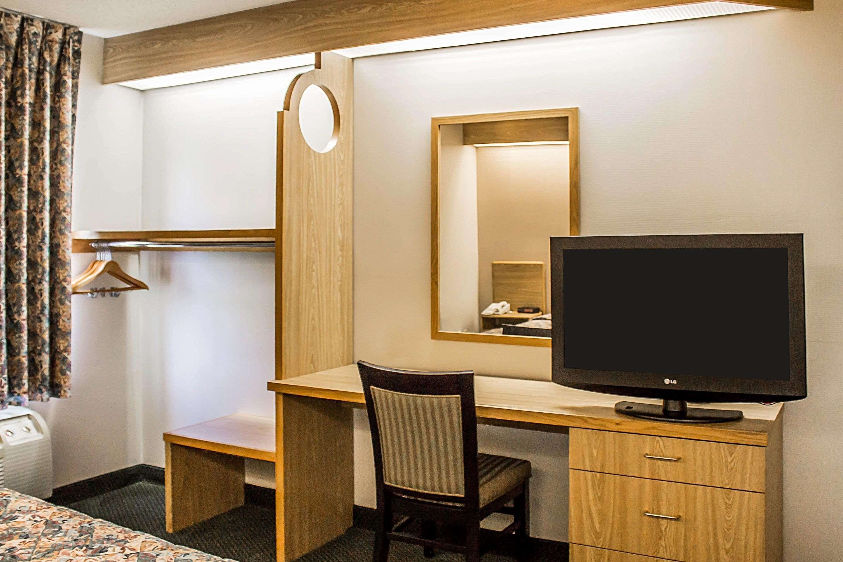 Ein Hotelzimmer mit einem Holztisch, einem Sessel, einem Fernseher, einem Spiegel, einem Kleiderschrank und einem Bett.