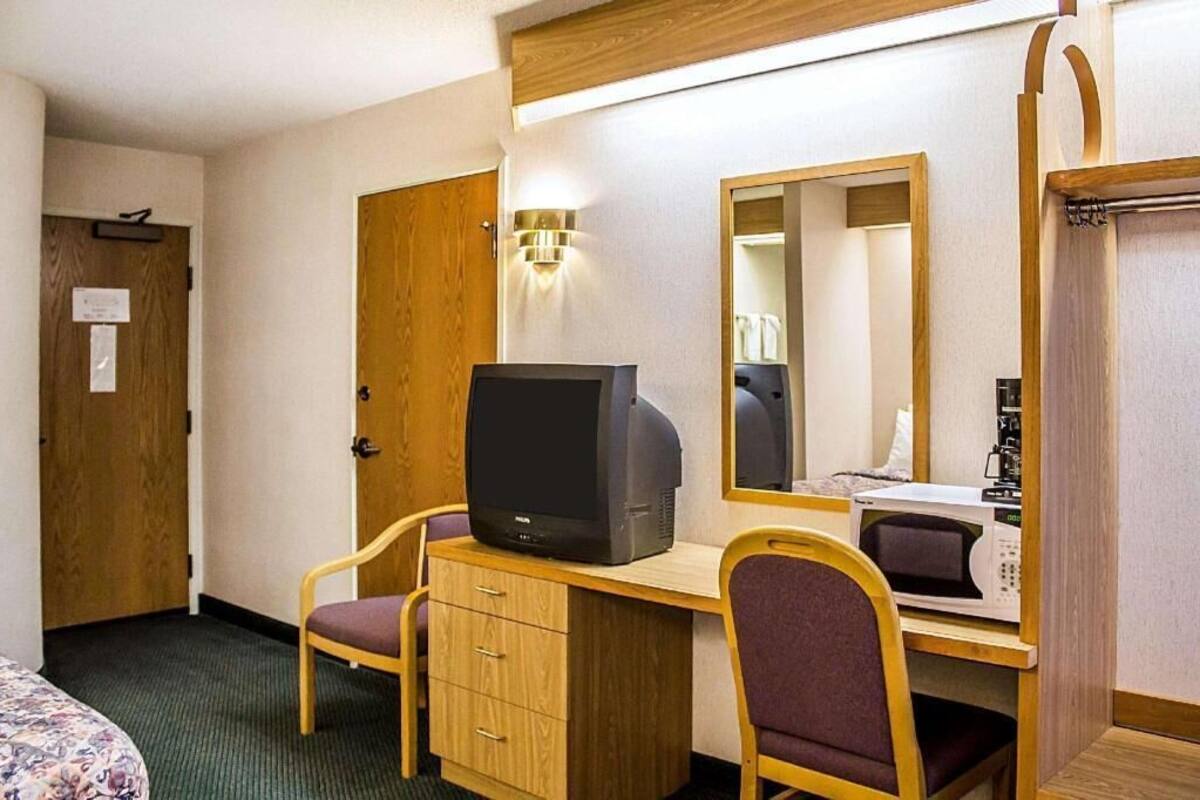 Quarto de hotel com uma escrivaninha de madeira, televisão, micro-ondas, espelho e guarda-roupa.