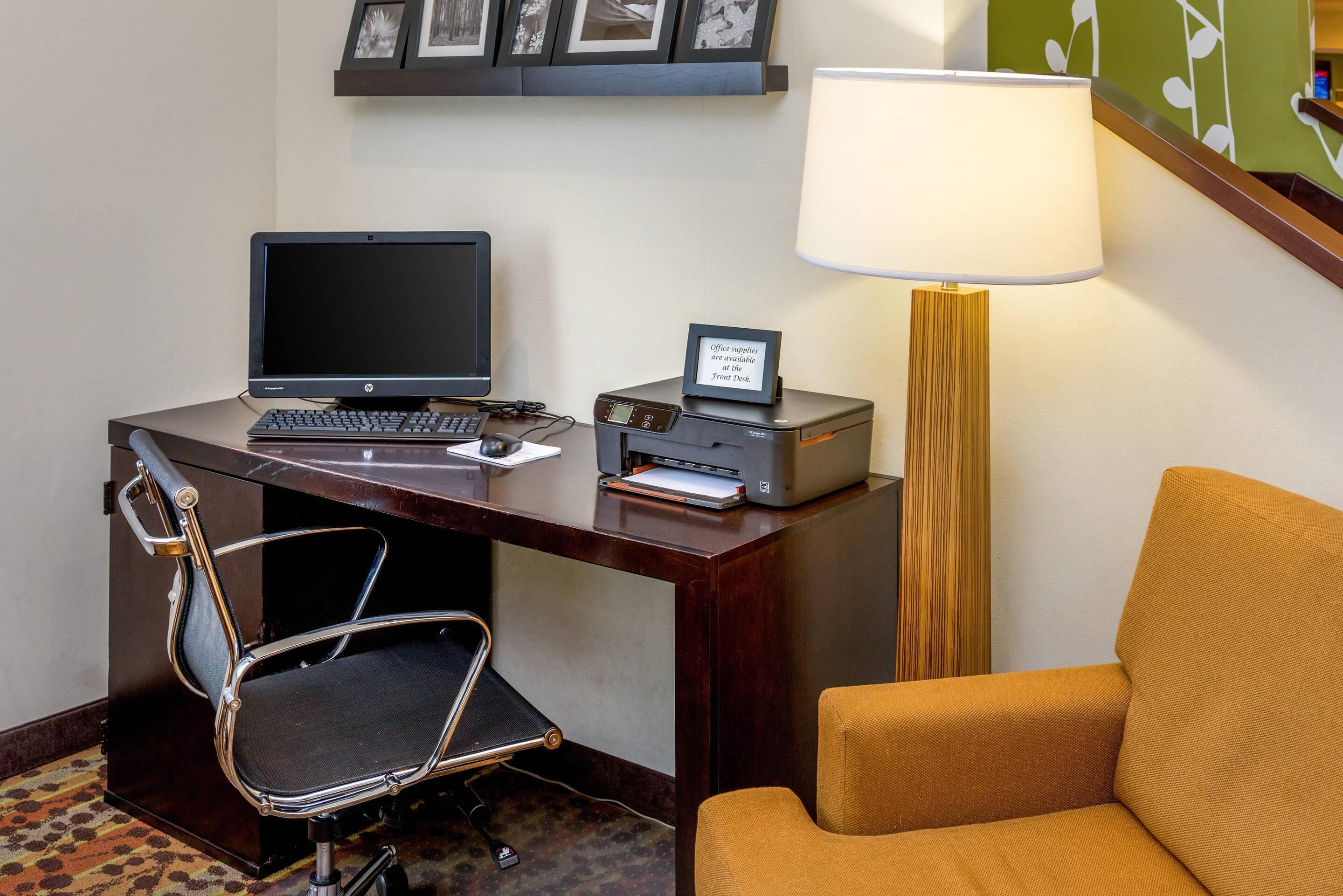 Habitación de hotel con escritorio, computadora, impresora, silla, lámpara y sofá.