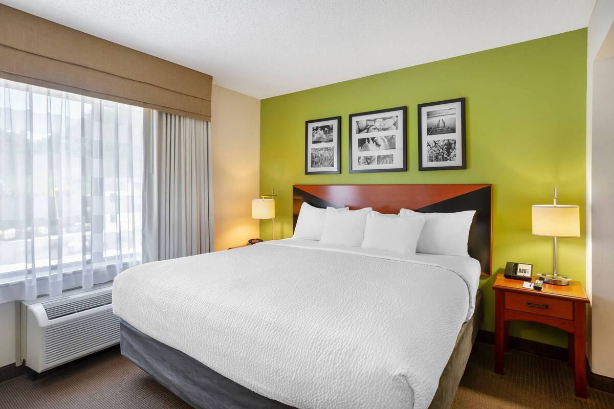 A hotel room with a large bed, two bedside tables with lamps, a wall-mounted air conditioner, and three framed pictures on the wall.