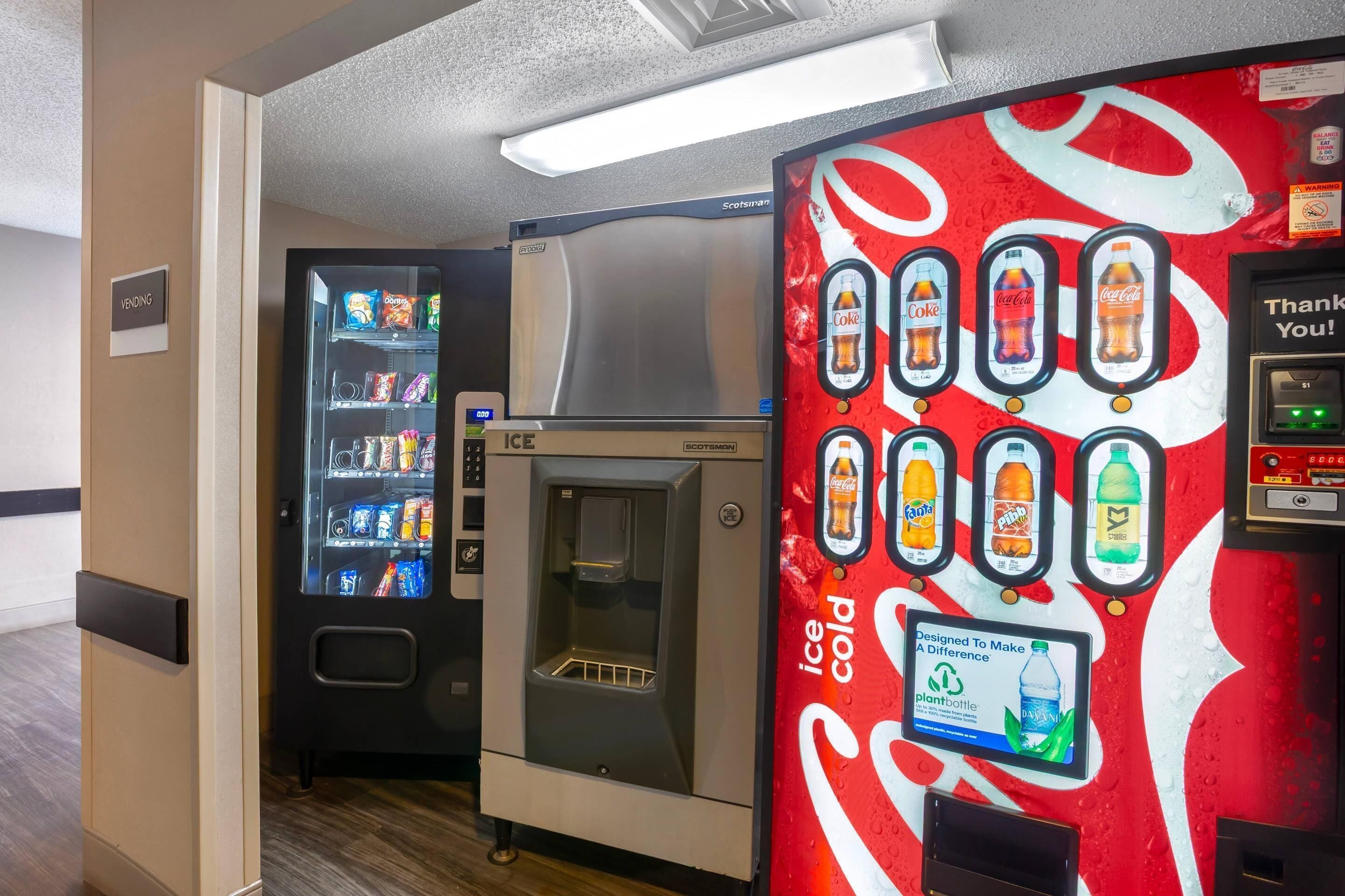 Ein Getränkeautomat mit Coca-Cola-Werbung, ein Eisautomat und ein Getränkespender mit verschiedenen Auswahlmöglichkeiten.