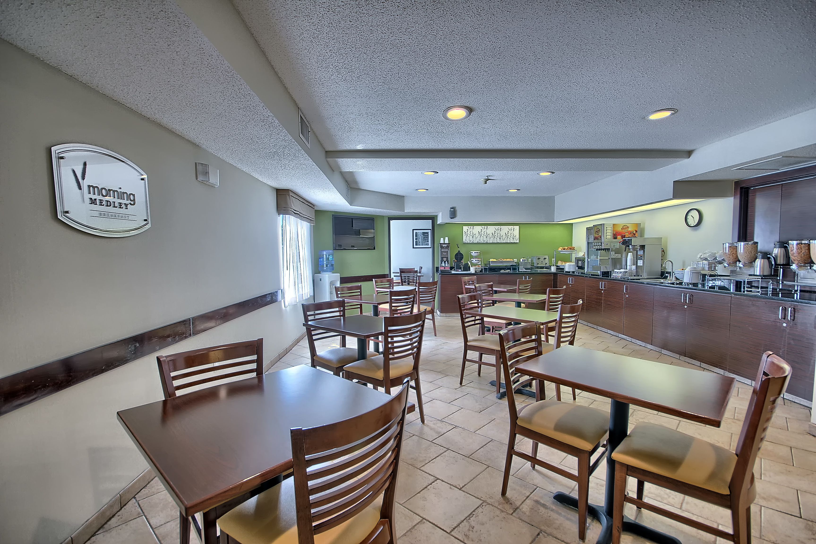 A restaurant with wooden tables and chairs, a kitchen area, and a clock on the wall.