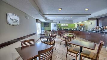 A restaurant with wooden tables and chairs, a kitchen area, and a clock on the wall.