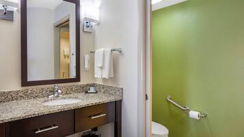 A bathroom with a granite countertop sink, a mirror, a towel rack, and a toilet with a grab bar.
