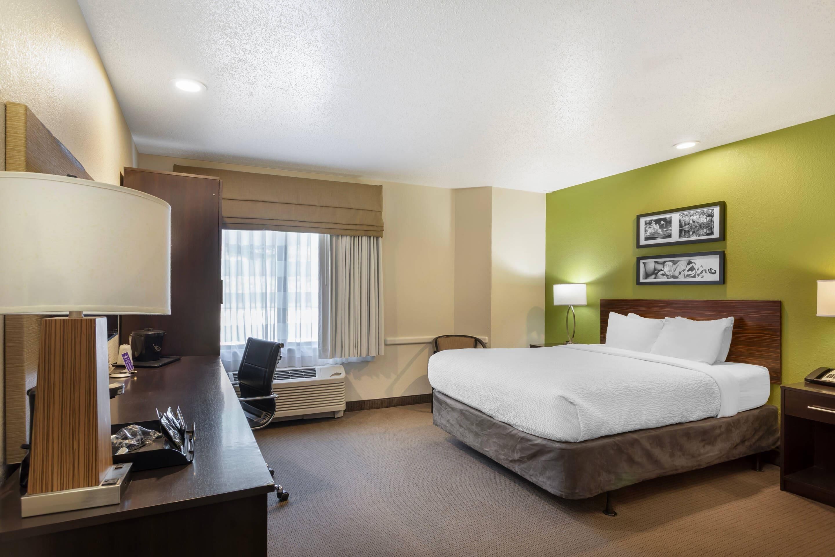 A hotel room with a bed, desk, chair, lamp, and a window with curtains.