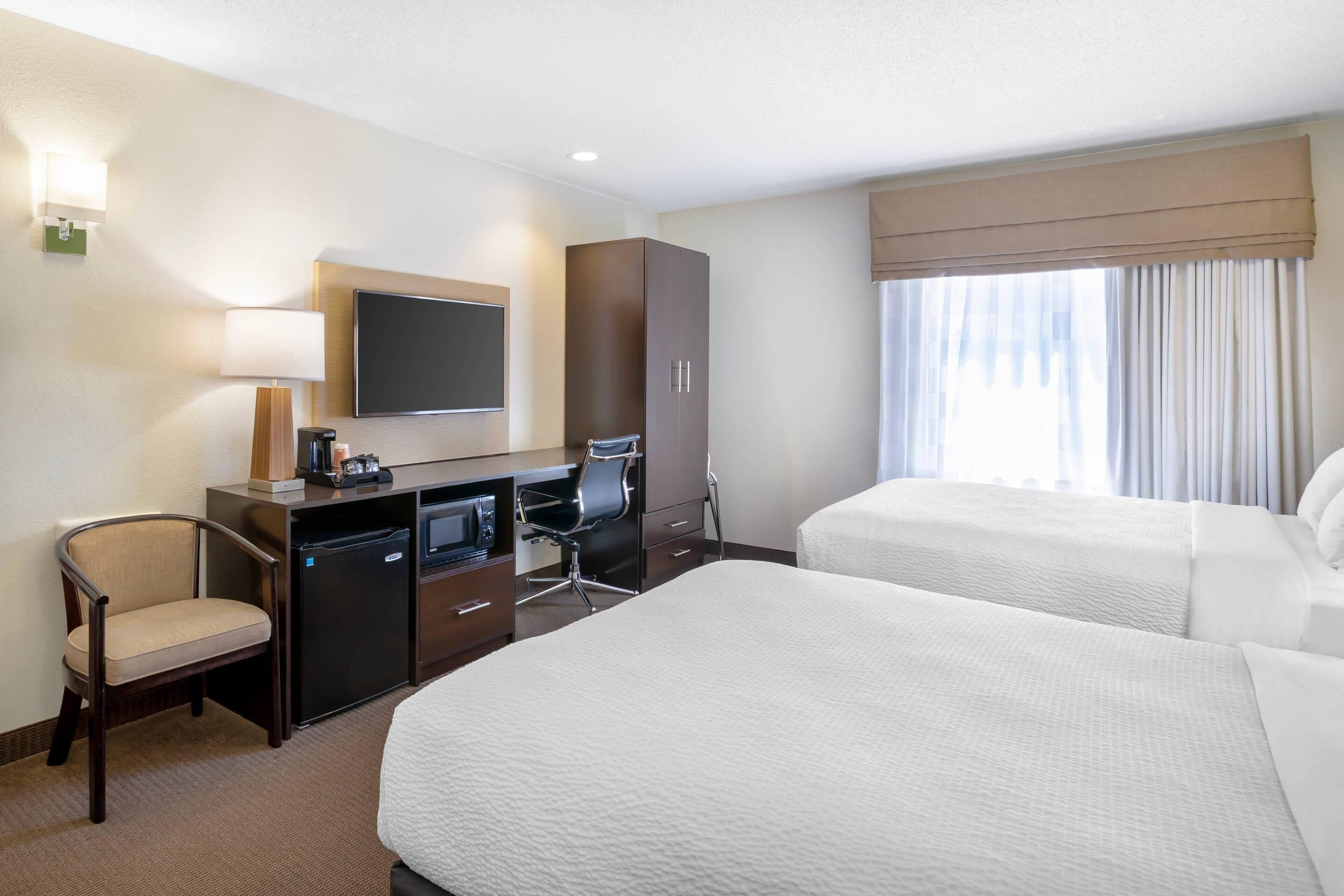 A hotel room with a bed, desk, chair, TV, minibar, and a window with curtains.