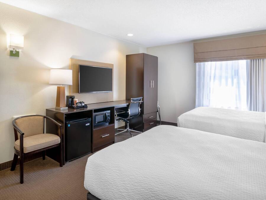 A hotel room with a bed, desk, chair, TV, minibar, and a window with curtains.