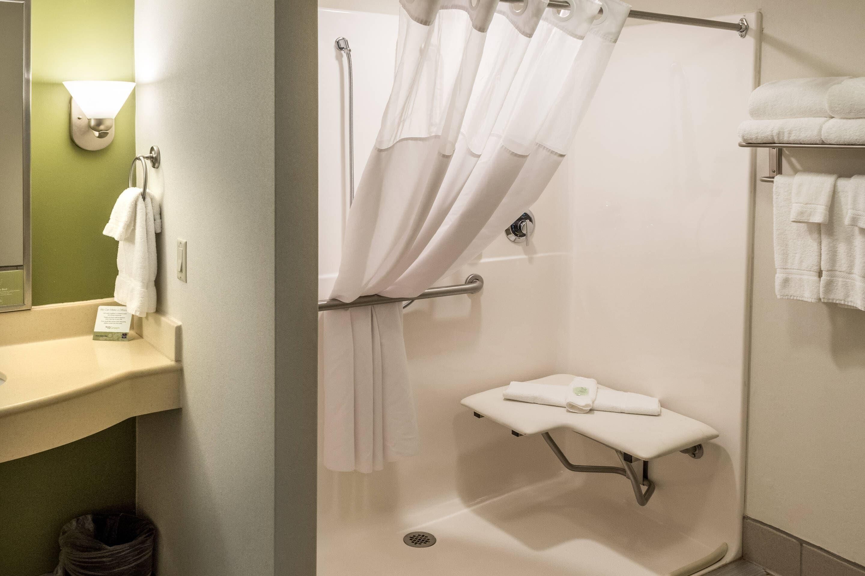 A bathroom with a shower, a sink, a towel rack, and a small shelf with a towel.