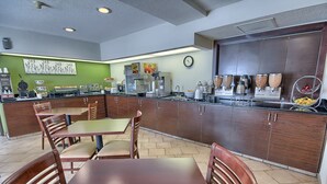 A restaurant with wooden tables and chairs, a kitchen area with various appliances, and a green wall with artwork.