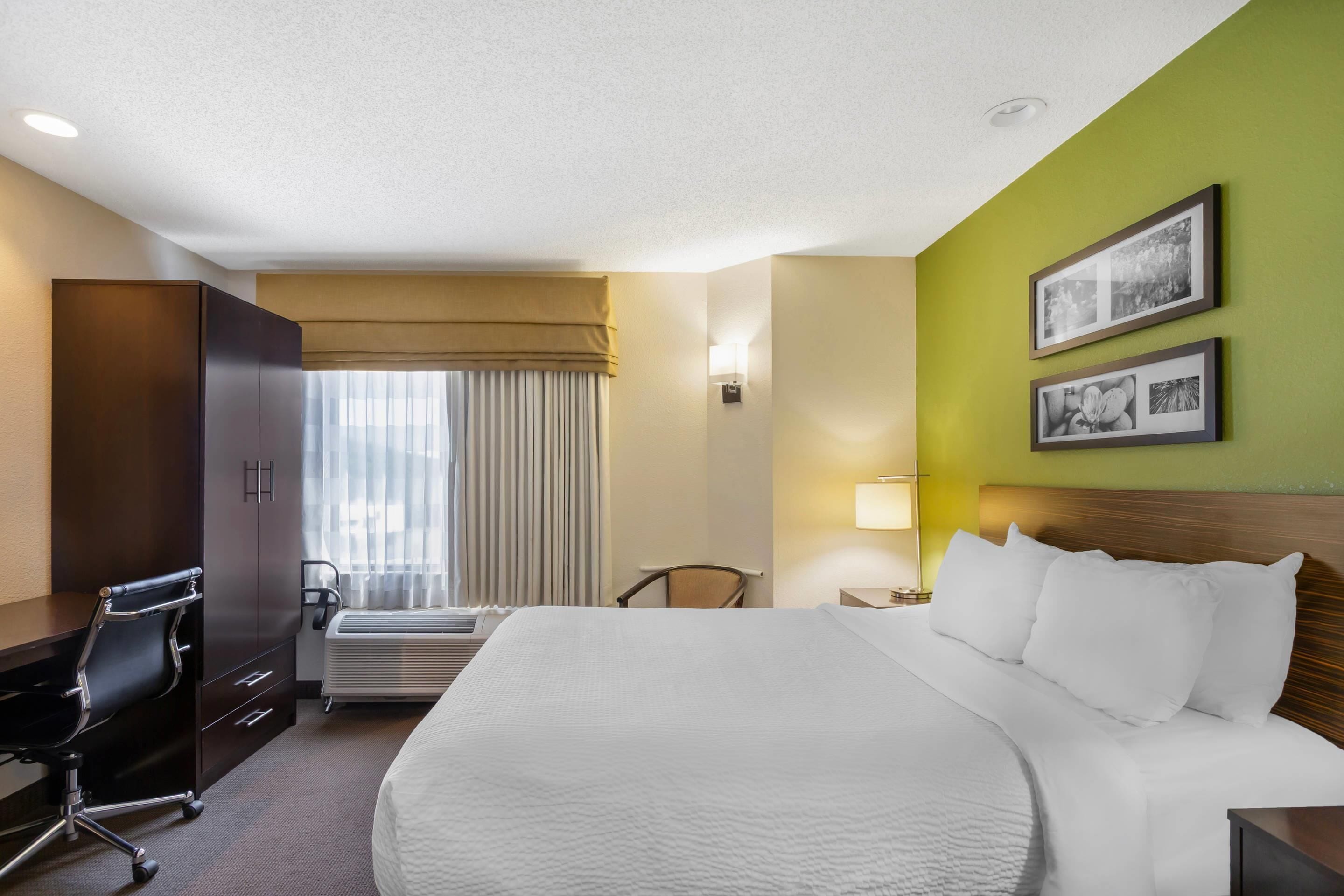 Habitación de hotel con una cama grande, un escritorio, una silla, una ventana con cortinas y cuadros en la pared.
