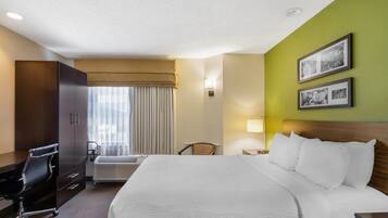 Habitación de hotel con una cama grande, un escritorio, una silla, una ventana con cortinas y cuadros en la pared.