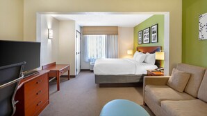 A hotel room with a bed, a desk, a TV, a sofa, and a wall with framed pictures.