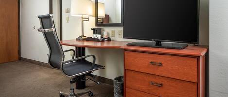 Habitación de hotel con escritorio, silla, televisor, lámpara y espejo.