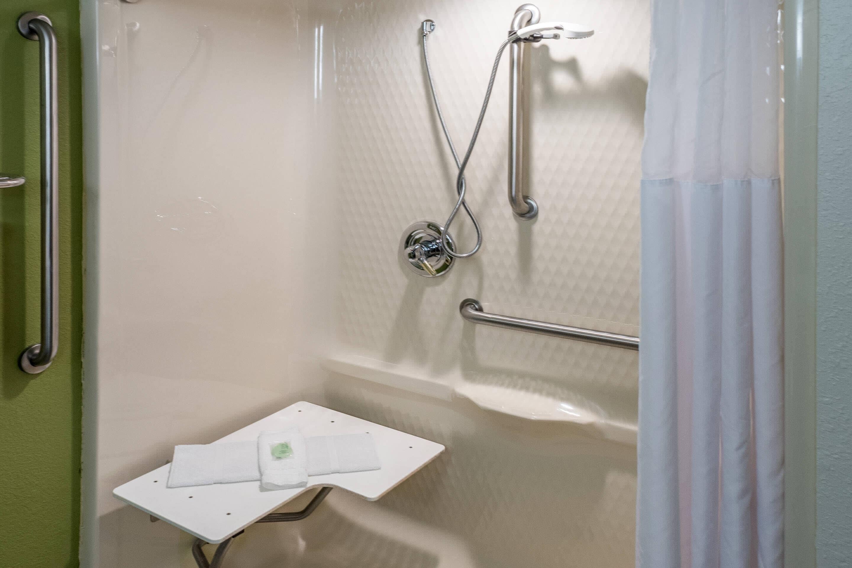 A shower area with a grab bar, a handheld showerhead, and a small white shelf with a towel.