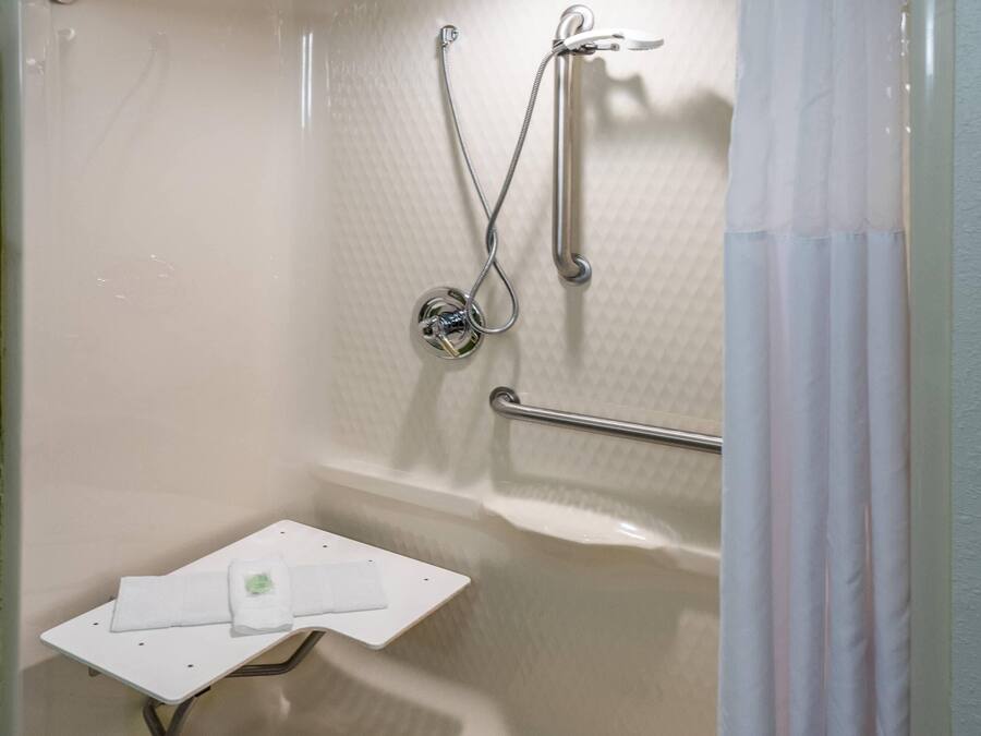 A shower area with a grab bar, a handheld showerhead, and a small white shelf with a towel.