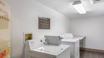 A laundry area with two washers and dryers, a sign for guest laundry, and a wall-mounted shelf with cleaning supplies.