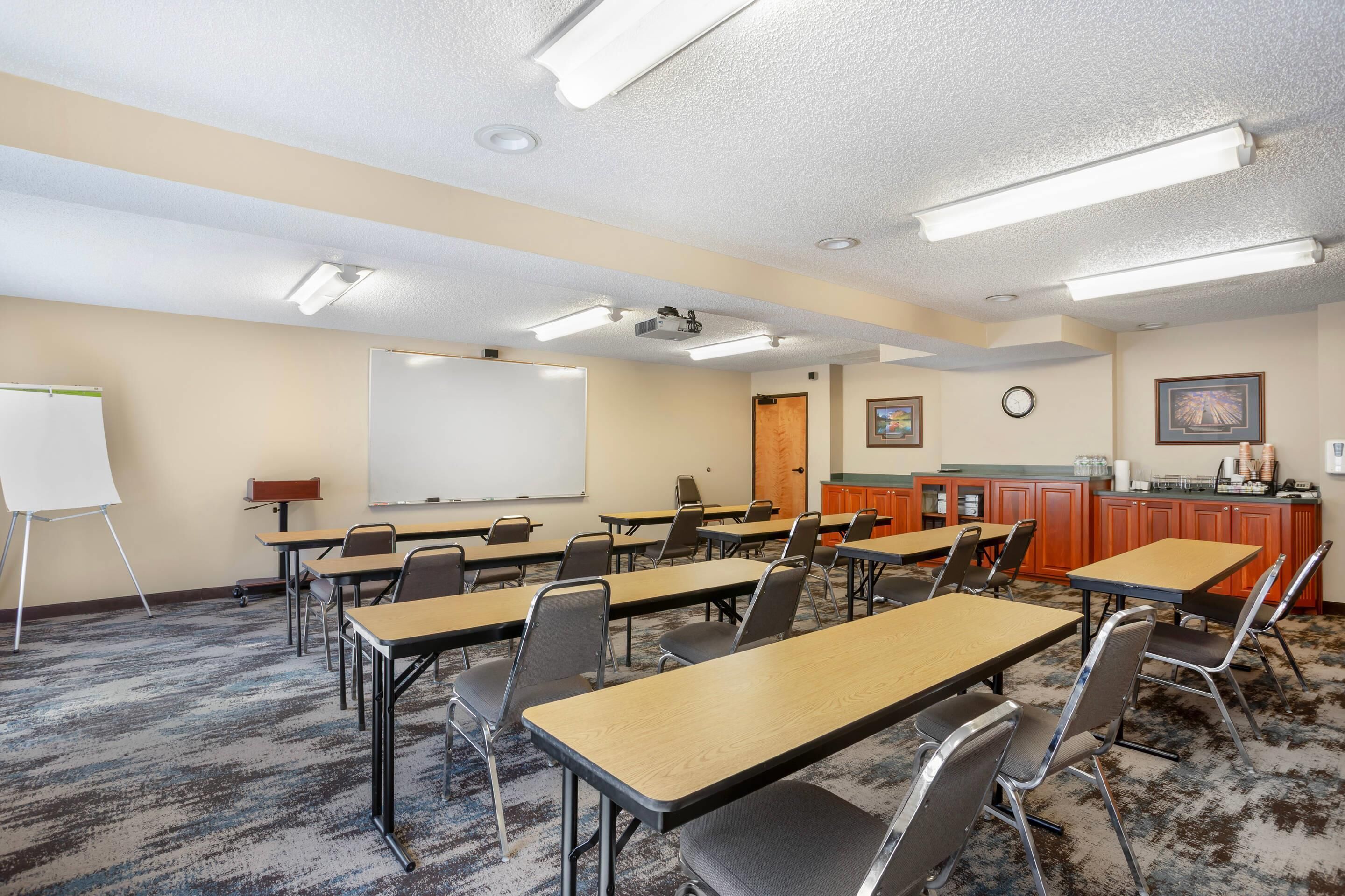 A conference room with tables, chairs, a whiteboard, a projector, and a clock on the wall.