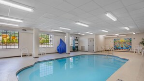 An indoor swimming pool with clear water, white walls, and ceiling lights.