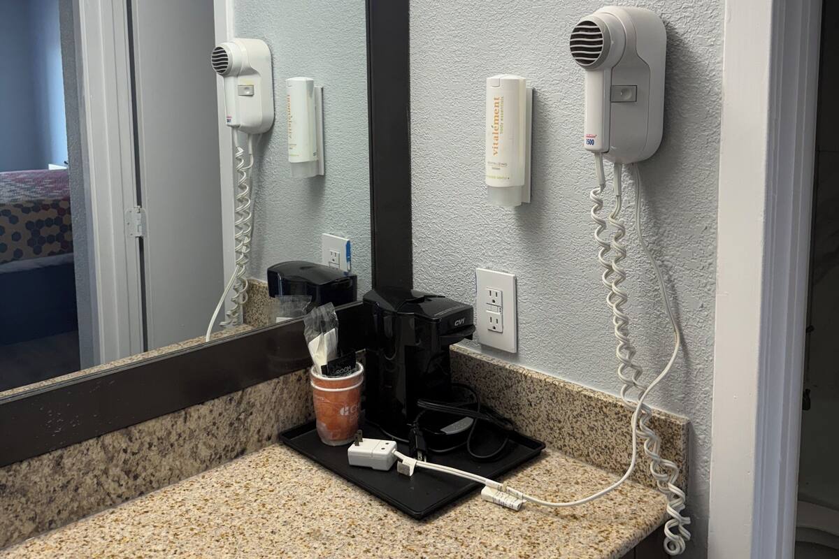 A bathroom with a granite countertop, a coffee maker, a hair dryer, and a mirror.