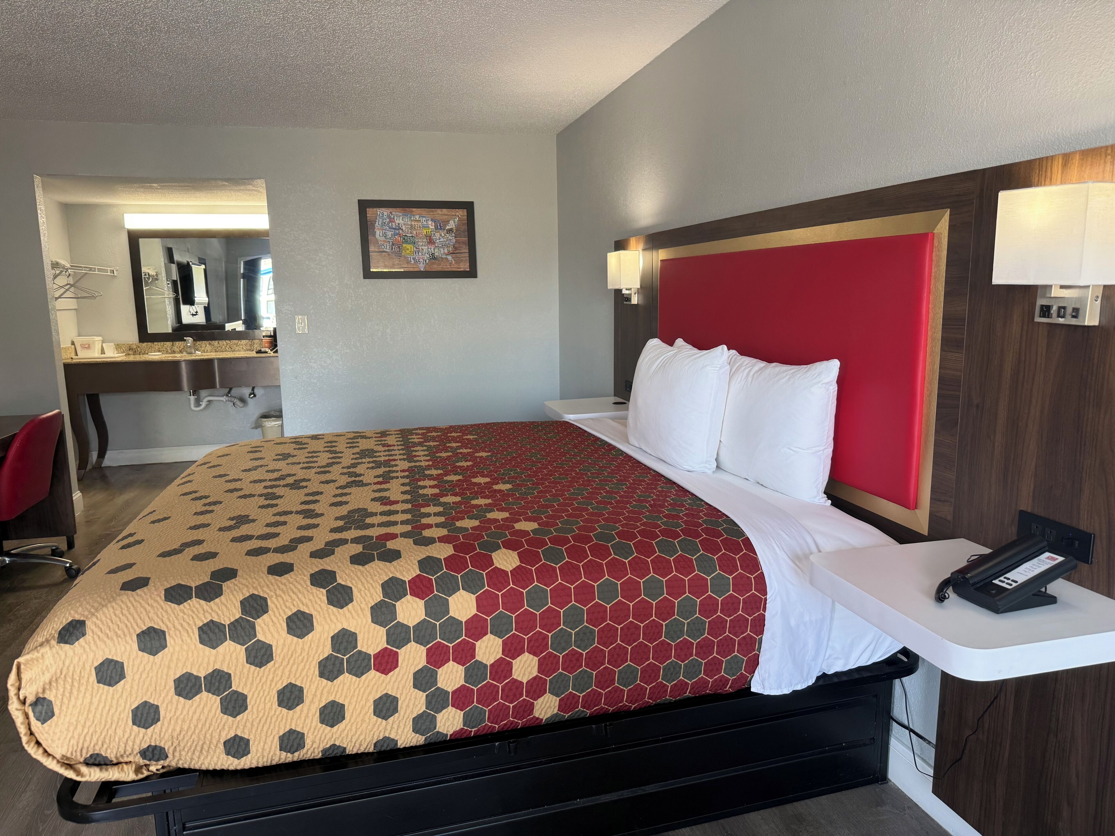 Ein Hotelzimmer mit Bett, Schreibtisch, Spiegel und einem Wandbild.