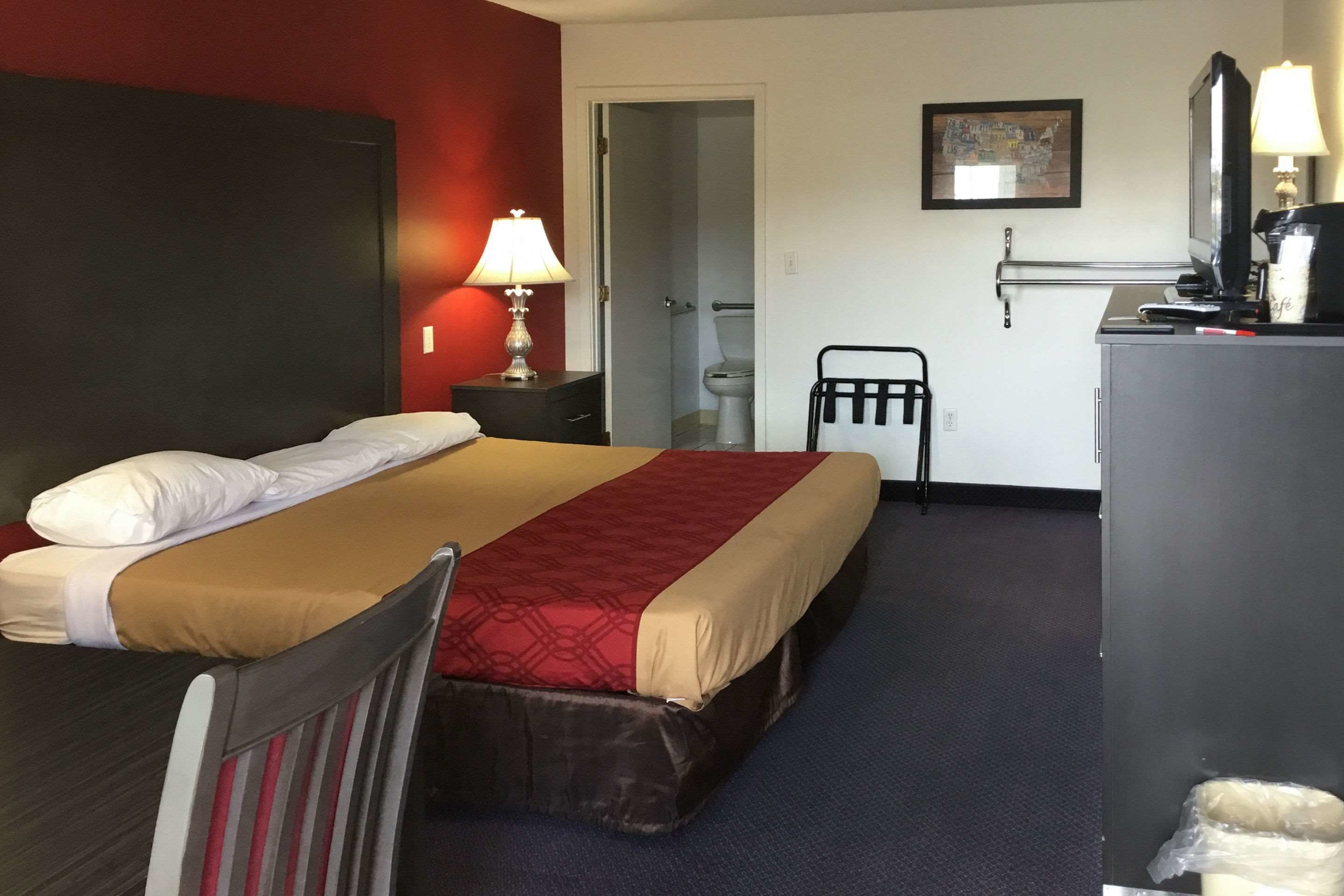 Een hotelkamer met een bed, een bureau, een stoel, een lamp, een televisie en een schilderij aan de muur.