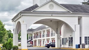 A motel with a central archway, multiple rooms, and a red roof.