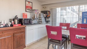 A kitchen area with a microwave, coffee machine, and a display case. There are red chairs and a window with blinds.