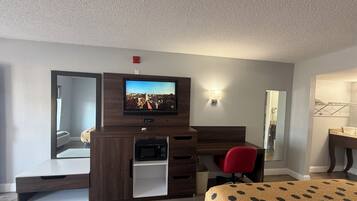 Une chambre d’hôtel équipée d’une télévision, d’un bureau, d’un four à micro-ondes, d’une chaise rouge et d’un lit recouvert d’une couverture à motifs.