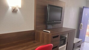 A hotel room with a wooden desk, a red office chair, a flat-screen TV, a microwave, and a small refrigerator.