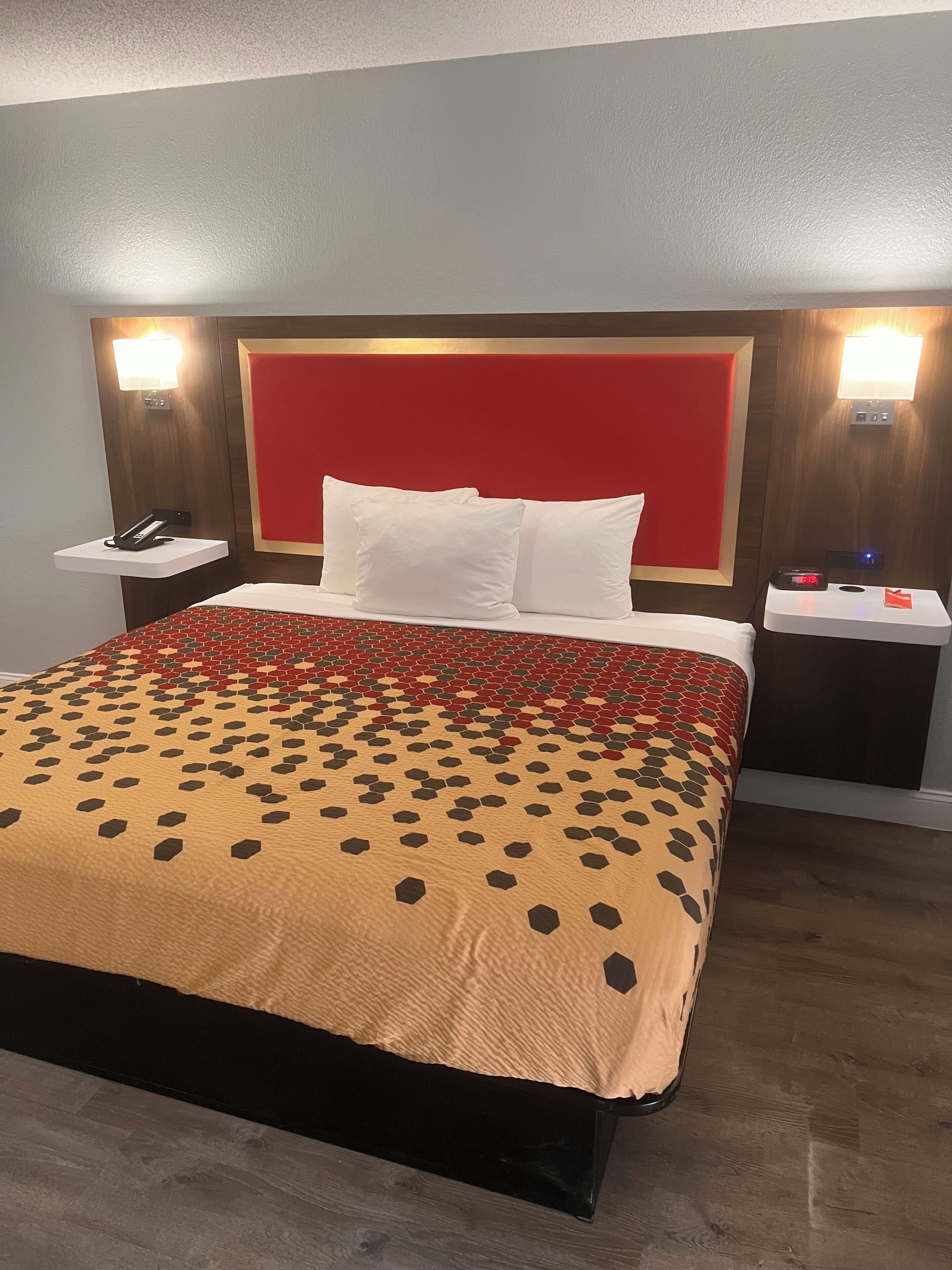 Une chambre d’hôtel avec un grand lit, une tête de lit rouge, des tables de chevet avec des lampes et une horloge.