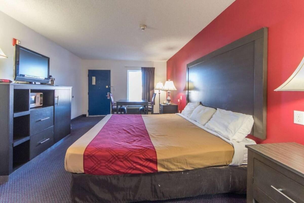 A hotel room with a bed, a desk, a chair, a TV, and a lamp.