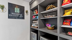 Un MainStay Marketplace con estantes llenos de refrigerios y bebidas, una planta pequeña y un logotipo en la pared.