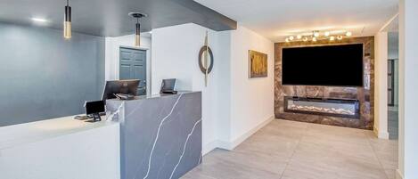 A modern reception area with a marble reception desk, a flat-screen TV mounted on a stone wall, and a minimalist decor including a wall-mounted circular art piece.