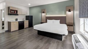 Una habitación de hotel moderna con cama, kitchenette y un ventanal grande.
