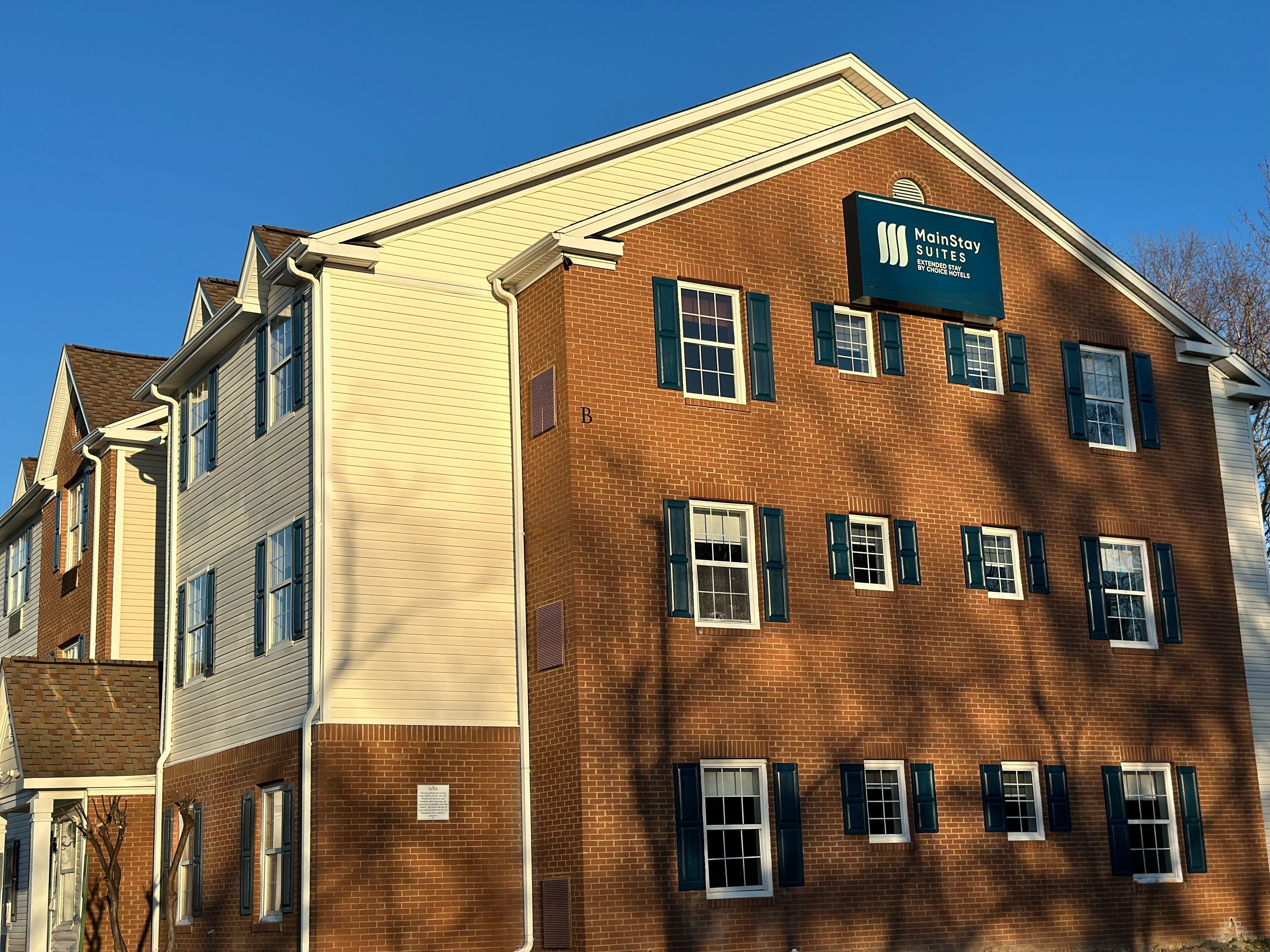 A two-story building with a sign for MainsStay Suites, indicating it is part of the extended family by Choice Hotels.