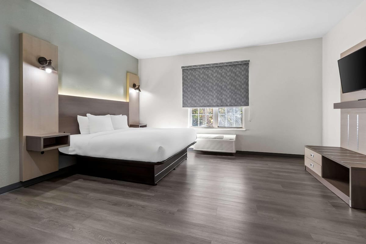 A modern bedroom with a large bed, bedside tables, a TV, and a window with blinds.