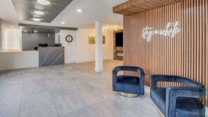 Una moderna zona de recepción con un mostrador de mármol, dos sillas azul oscuro, un letrero de neón y una pared de listones de madera.