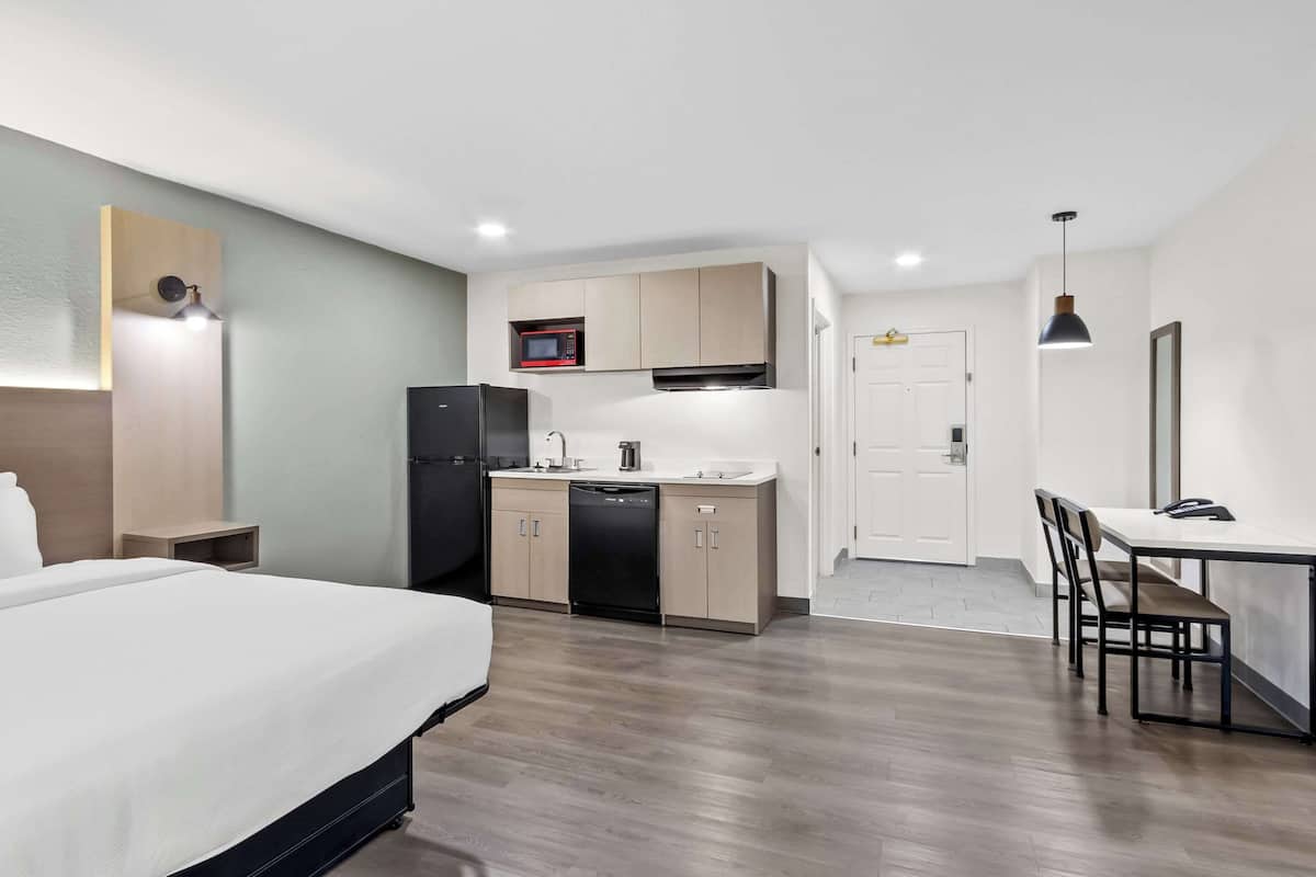 A compact hotel room with a bed, kitchenette, and a dining area.